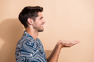 Poster - Profile side photo of cheerful nice man dressed stylish clothes looking empty space presenting novelty isolated on beige color background