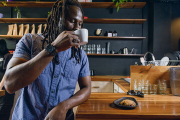 black man with dreadlocks customer in restaurant standing drinking and enjoying cup of coffee