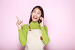 © Parichat - Standing and pointing happily, Portrait of a beautiful young woman in a light pink background, happy and smile, Young woman wearing an apron