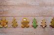 Glazed gingerbread cookies in the form of men and Christmas trees lie in a row in the center of a wooden table