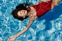 Young Woman In The Pool In A Red Swimsuit With A Beautiful Smile Lying On The Water And Swimming In The Sun Swimming In The Pool, The Concept Of Relaxing On Vacation.
