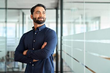 Wall Mural - Confident bearded Indian business man leader looking away standing in office hallway. Professional businessman manager executive or male employee, investor entrepreneur thinking of future success.