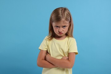 Wall Mural - Resentment. Angry little girl with crossed arms on light blue background