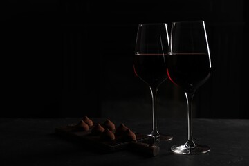 Wall Mural - Glasses of red wine and chocolate truffles on black table in darkness, space for text