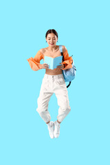 Canvas Print - Portrait of young female student with book jumping against blue background