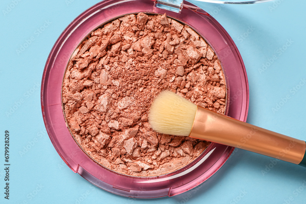 Makeup brush and highlighter on blue background