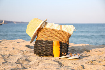 Stylish beach bag, hat, flip-flops and sunscreen cream on sea beach