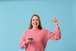 © Pixel-Shot - Beautiful woman with mobile phone pointing at something on blue background