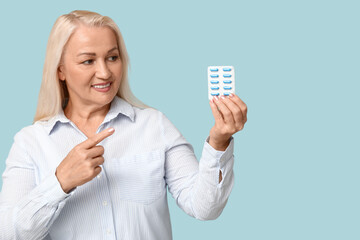 Canvas Print - Beautiful mature woman pointing at pills on blue background