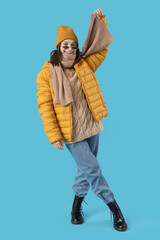 Wall Mural - Young woman in winter clothes on blue background