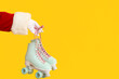 Santa Claus hand with roller skates on yellow background