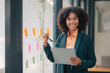 © amnaj - African american Businesswoman writing sticky note to her mirror at the office. Business woman brainstorming and working and writing on the glass board in office.