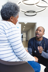 Wall Mural - African american male doctor talking with senior woman in hospital waiting room