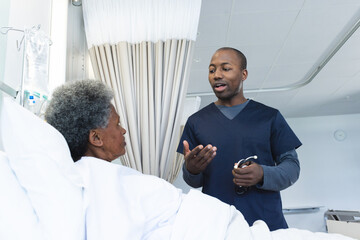 Wall Mural - African american male doctor talking with senior female patient in hospital room