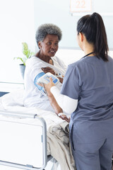 Wall Mural - Diverse female doctor testing blood pressure of senior female patient in hospital room