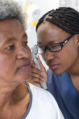 Wall Mural - African american female doctor testing ear of senior female patient in hospital room