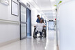 © WavebreakMediaMicro - African american female doctor walking with senior female patient in wheelchair in hospital corridor