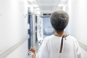 Wall Mural - Back of african american senior female patient with drip walking in hospital corridor