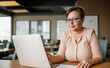 © Celt Studio - adult plus-size woman sits at desk in modern coworking office and waits for negotiations with client. businesswoman working on laptop, successful confident executive manager sitting at office desk