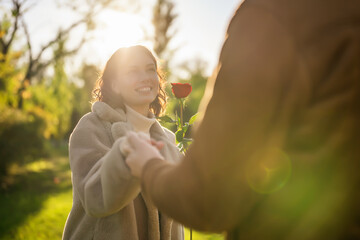 Wall Mural - Portrait of happy loving couple in park in sunset. Man is giving rose to his woman.