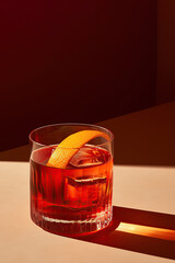 Negroni cocktail in a cut-crystal glass, garnished with an orange peel at the  table with shadow.