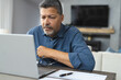 © Wavebreak Media - Busy senior biracial man holding glasses and working on laptop at home