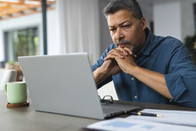 Busy senior biracial man thinking and working on laptop at home