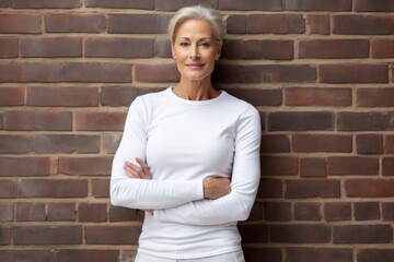 Canvas Print - Portrait of a content woman in her 60s sporting a long-sleeved thermal undershirt against a vintage brick wall. AI Generation