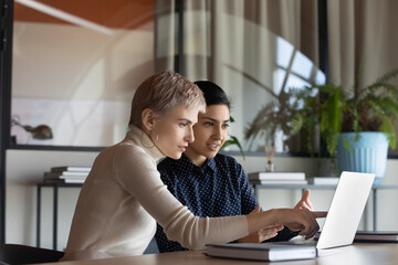 Canvas Print - Corporate teacher showing new employee learning video at laptop, company mentor training intern. Diverse coworkers watching presentation, reading message, working together at computer