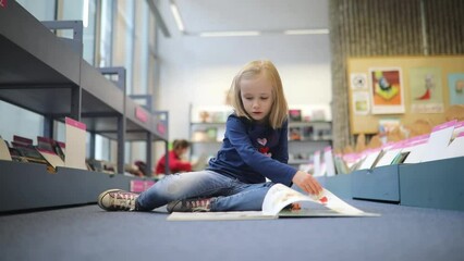 Wall Mural - Adorable preschooler girl sitting on the floor in municipal library and reading book