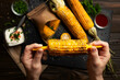 Grilled corn on the cob in caucasian hands on kitchen wooden table background