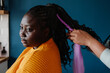 © gstockstudio - Close-up of hairdresser braiding hair to young African woman in salon