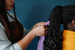 © gstockstudio - Close-up of African hairdresser braiding hair to female customer on blue background