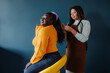 © gstockstudio - Concentrated African hairdresser braiding hair to smiling female customer on blue background