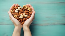  Two Hands Holding A Handful Of Nuts In The Shape Of A Heart On A Blue Wooden Background, Top View, Copy - Up, With Copy Space For Text.