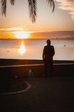 Fototapeta  - persona con su perro a la orilla del mar contemplando el amanecer