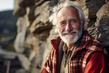 Wall Mural - Portrait of a grinning man in his 70s dressed in a relaxed flannel shirt against a rocky cliff background. AI Generation