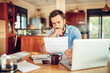 © Geber86 - Young man looking at paper document with concern at home