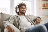 Fototapeta Panele - Joyful man on a sofa at the window, listening music with a headphones.