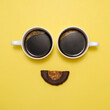 Coffee creative happy emoji. Smile from two cups of black espresso and healthy raw dessert as mouth. Smiley face with eyes on yellow background. Top view. Food that brings positive emotions