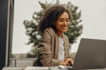 Smiling female freelancer working on laptop while sitting in cafe terrace. Distance work concept