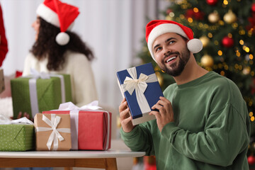 Wall Mural - Christmas celebration in circle of friends. Happy young man with gift box at home, selective focus