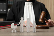Family law. Judge with gavel sitting at wooden table, focus on figure of parents and children