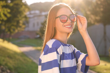 Poster - Beautiful smiling woman wearing sunglasses in park, space for text