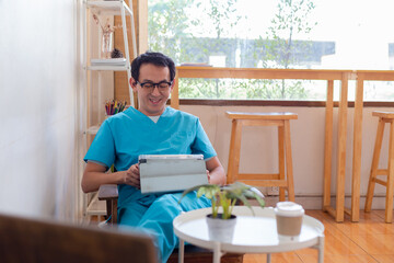 Smiling nurse using digital tablet in employee lounge. Happy nurse resting on couch in lounge area and drinking cup of coffee.