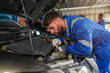 © kelvn - Mechanic working under the hood at the repair garage. Portrait of a happy mechanic man working on a car in an auto repair shop. Male mechanic working on car.