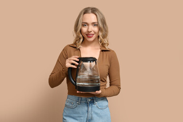 Wall Mural - Beautiful young woman with modern electric kettle on beige background