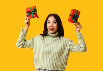 Wall Mural - Young Asian woman with Christmas gift boxes on yellow background