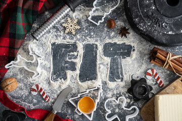 Healthy Christmas baking flat lay concept. Fit written in flour and dumbbell barbell weights, dough ingredients, cookie cutters. Fitness diet food preparation. Gym workout, sport training composition.