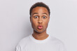 © wayhome.studio  - Photo of surprised African man with curly hair keeps lips folded and eyes windely opened cannot believe in shocking news dressed in casual t shirt isolated over white wall reacts to something shocking